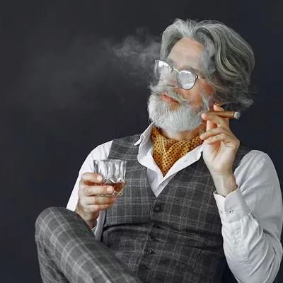 Gentleman sediaci s pohárom whisky a fajčiaci cigaru